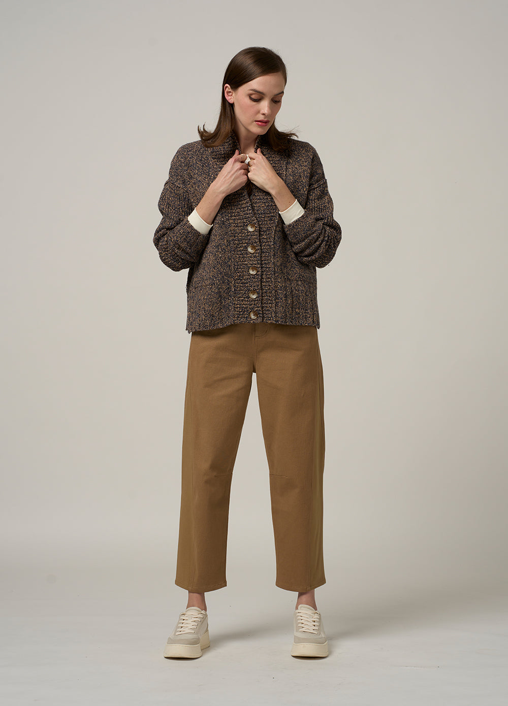 Woman wearing a brown textured cardigan and tan pants on a plain background