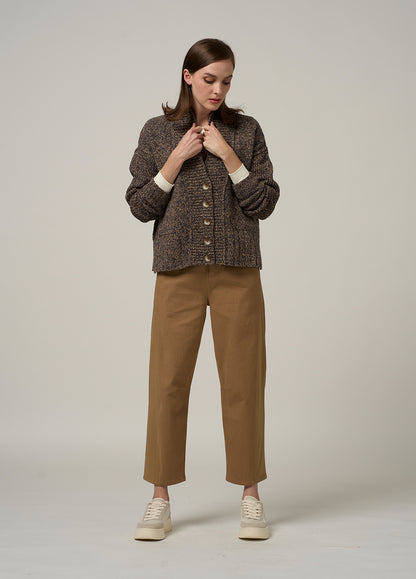 Woman wearing a brown textured cardigan and tan pants on a plain background
